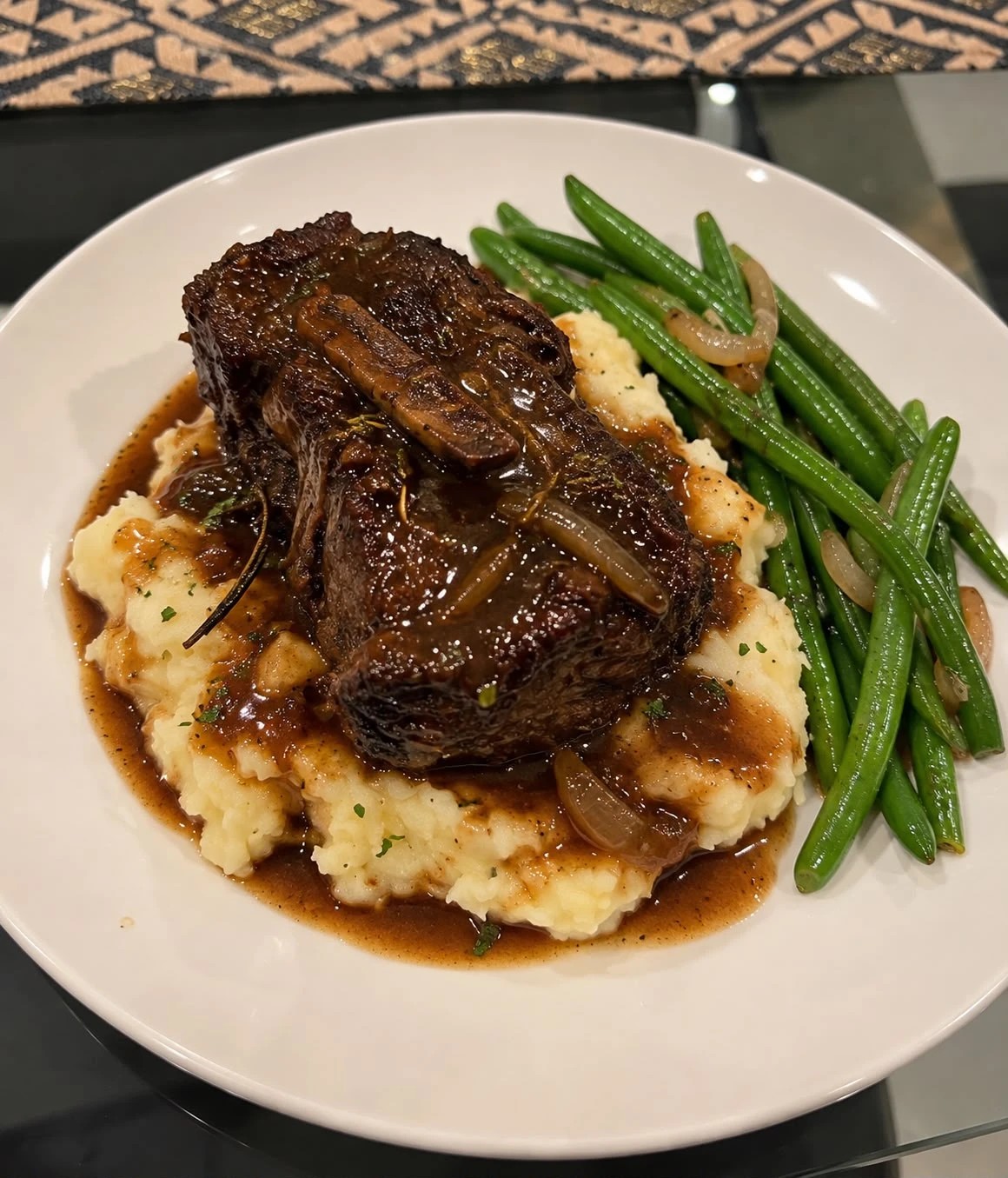 A braised short rib with onion gravy over mashed potatoes, with green beans